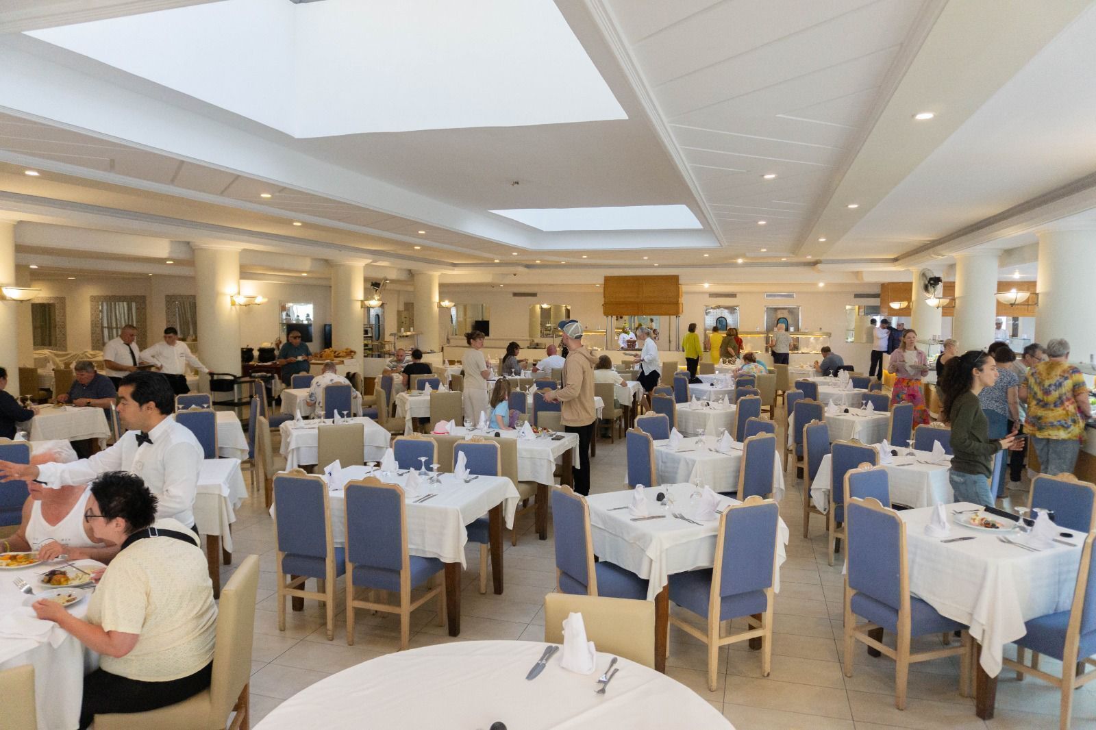 Un'ampia sala da pranzo con numerosi tavoli e sedie, soffitti alti con lucernari e un design d'interni moderno.