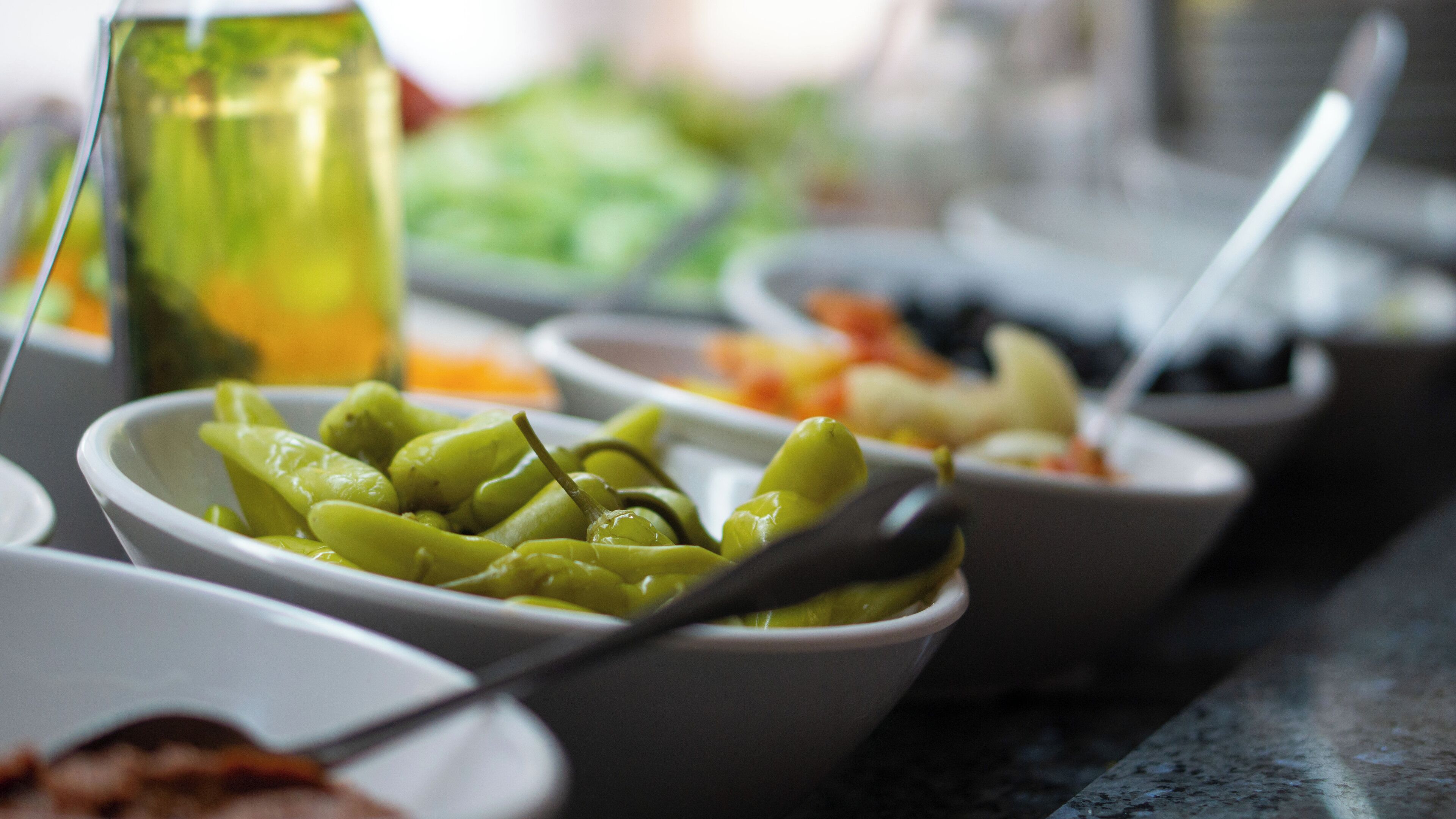 Una mesa de buffet con diversos platos, incluyendo un bol de verduras verdes y una botella de salsa.