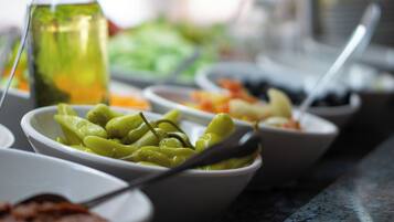 Una mesa de buffet con diversos platos, incluyendo un bol de verduras verdes y una botella de salsa.