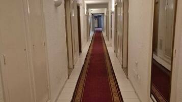 A long, narrow hallway with white walls and doors on both sides, leading to a room at the end.