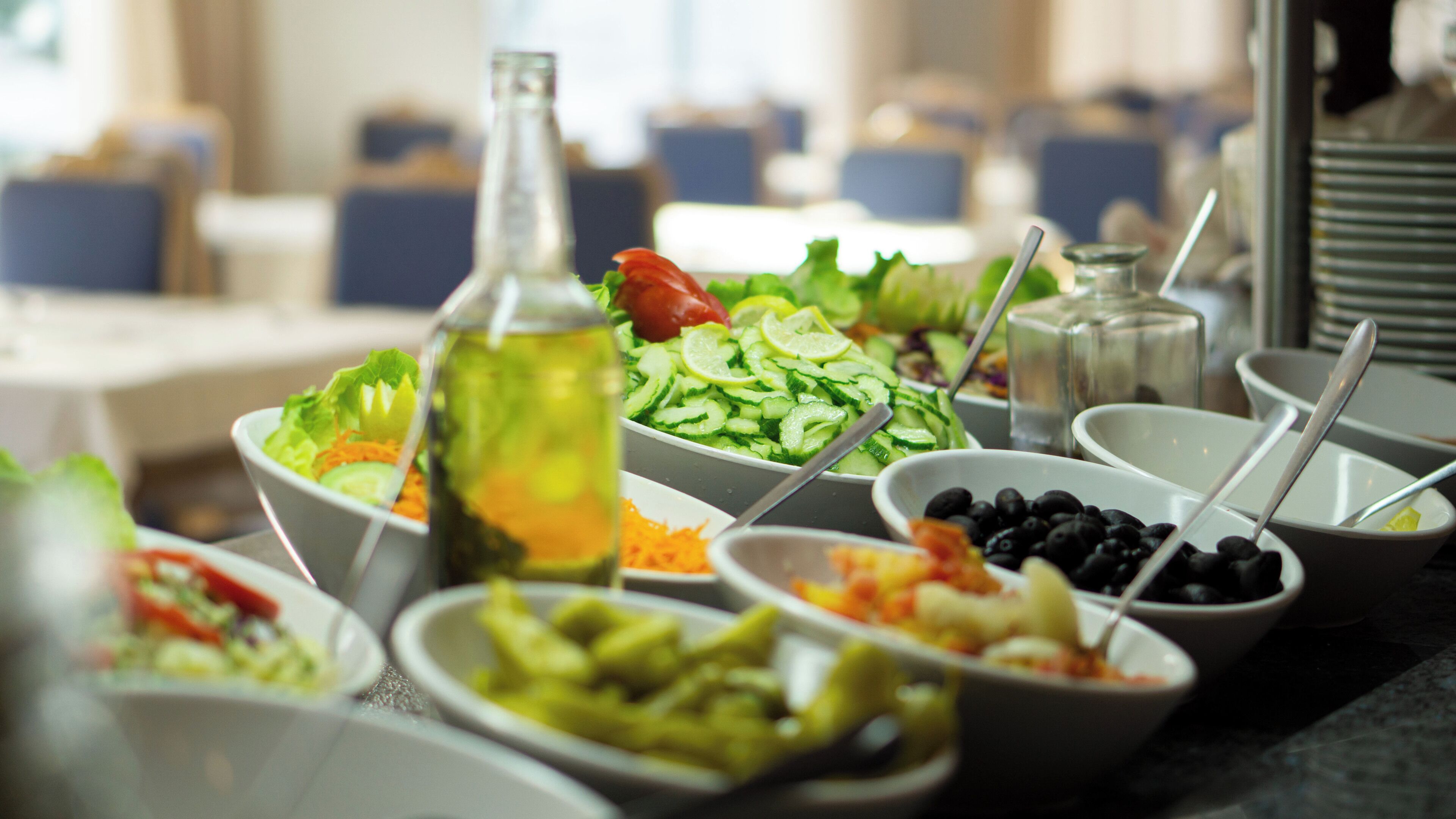 A buffet table with various dishes including salads, vegetables, and a bottle of oil.