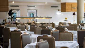 Ein Restaurant mit mehreren Tischen und Stühlen, einem Küchenbereich im Hintergrund und einer neutralen Farbgestaltung.