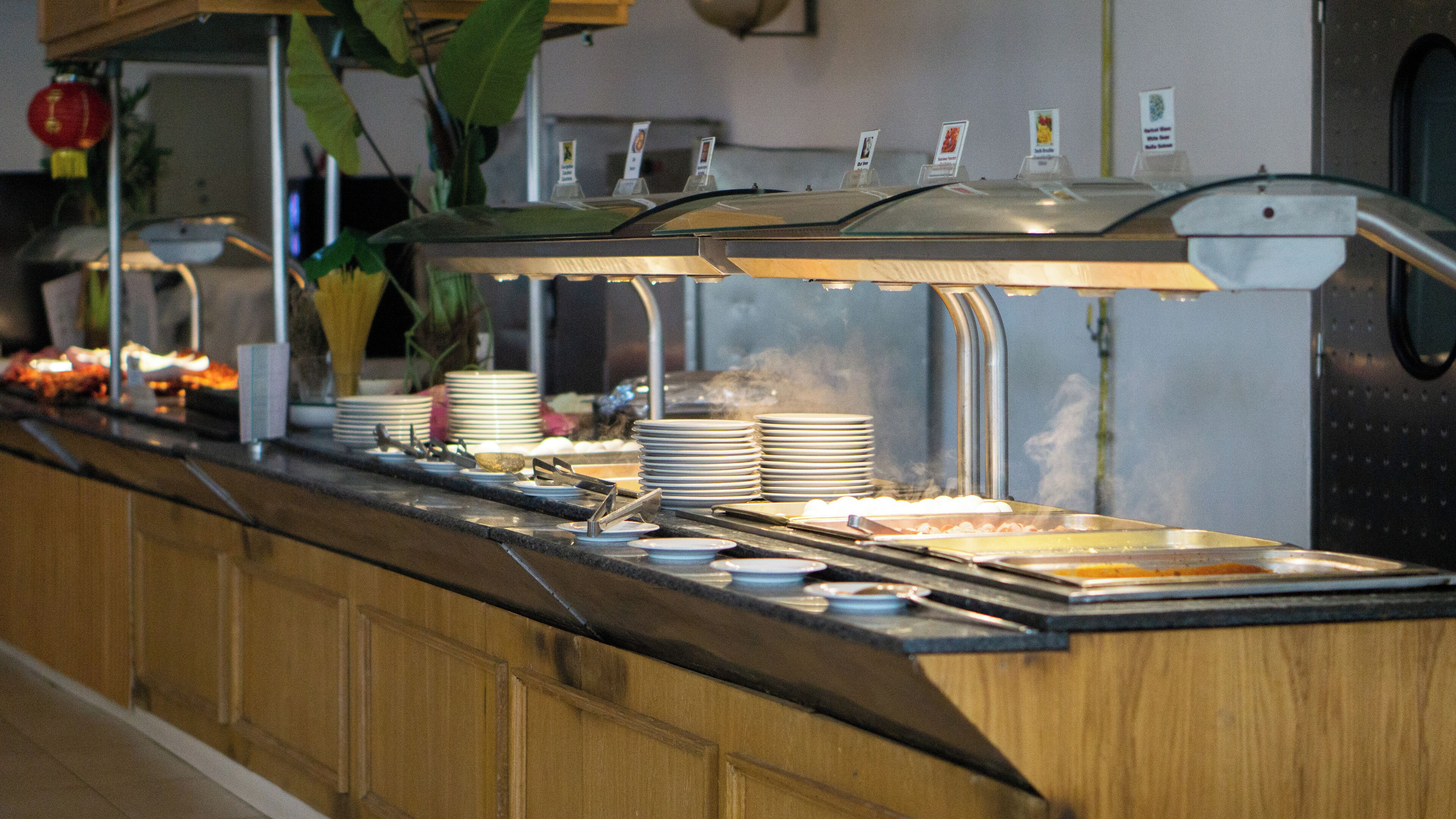 Un buffet avec plusieurs présentoirs de plats, des assiettes et des couverts.