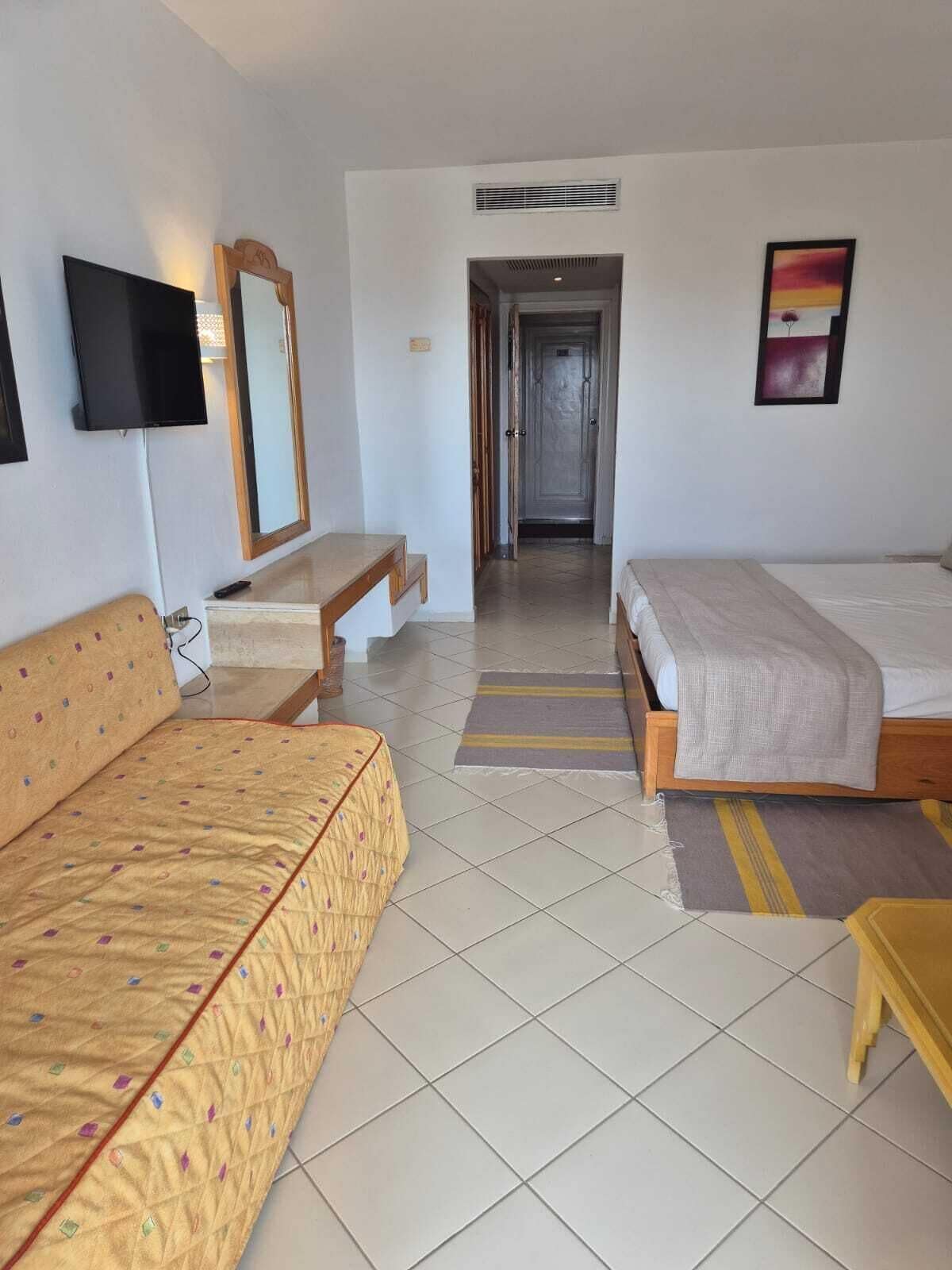 A hotel room with two beds, a TV, a mirror, and a painting.