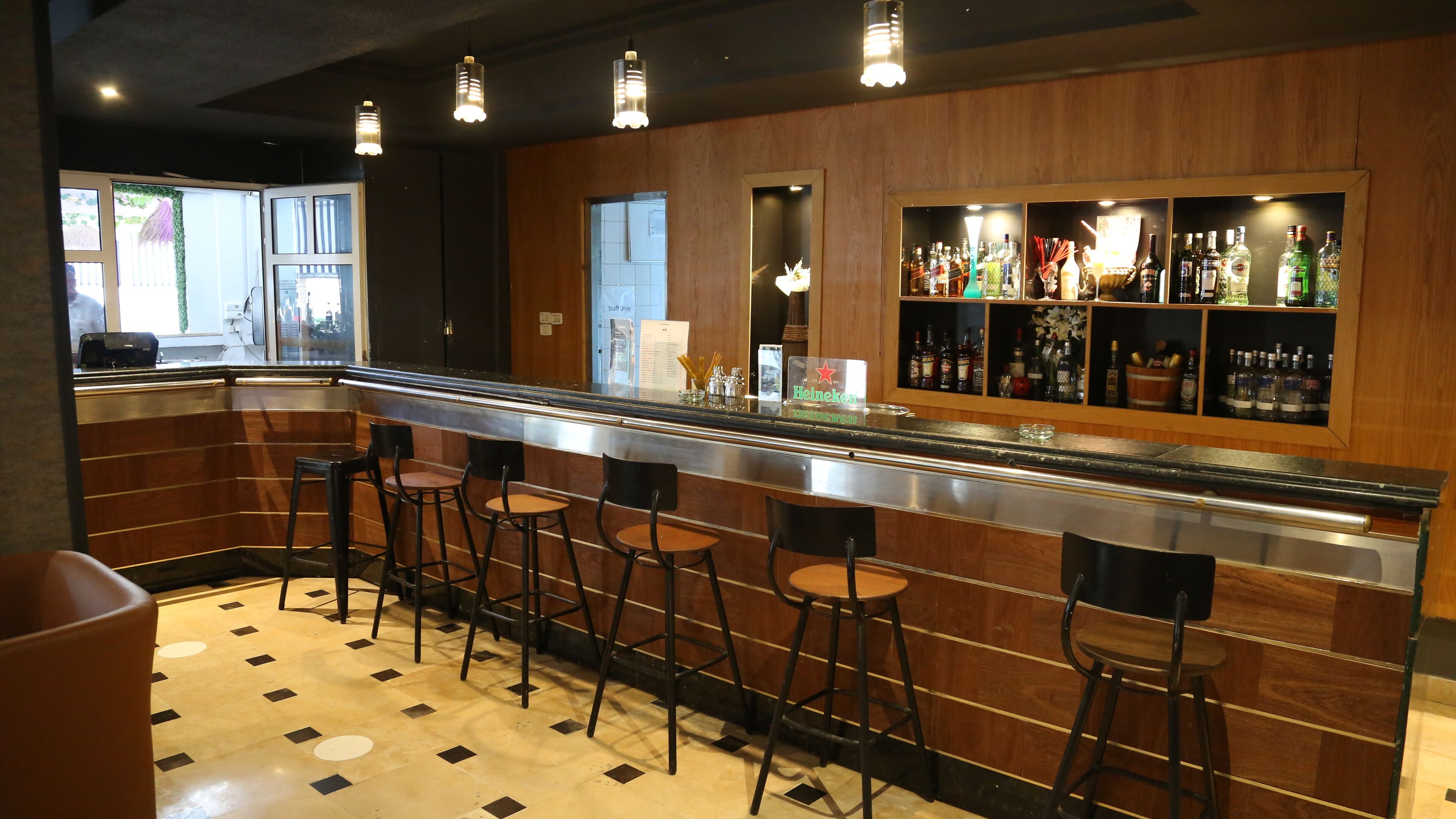 Eine Bar mit einer langen Theke, mehreren Barhocker und einer Auswahl an Spirituosenflaschen.