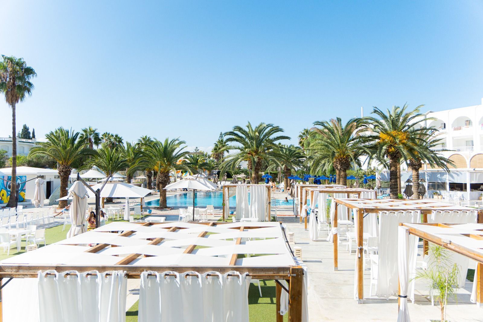 A poolside area with sun loungers, umbrellas, and palm trees.