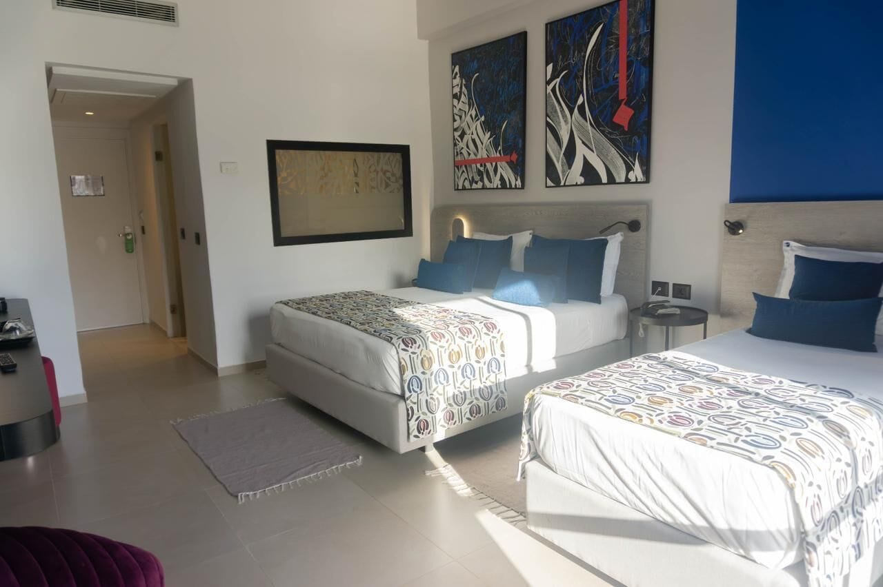 A hotel room with two beds, a large abstract painting, and a view of the outside.