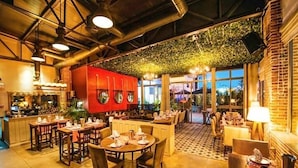 A restaurant with a high ceiling, exposed ductwork, and a red kitchen area. Tables are set with white tablecloths and silverware. - Golf Residence- Family Only (Port El Kantaoui)