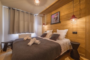 A wooden-paneled bedroom with a bed, pillows, a blanket, a bedside table, and a hanging light fixture.