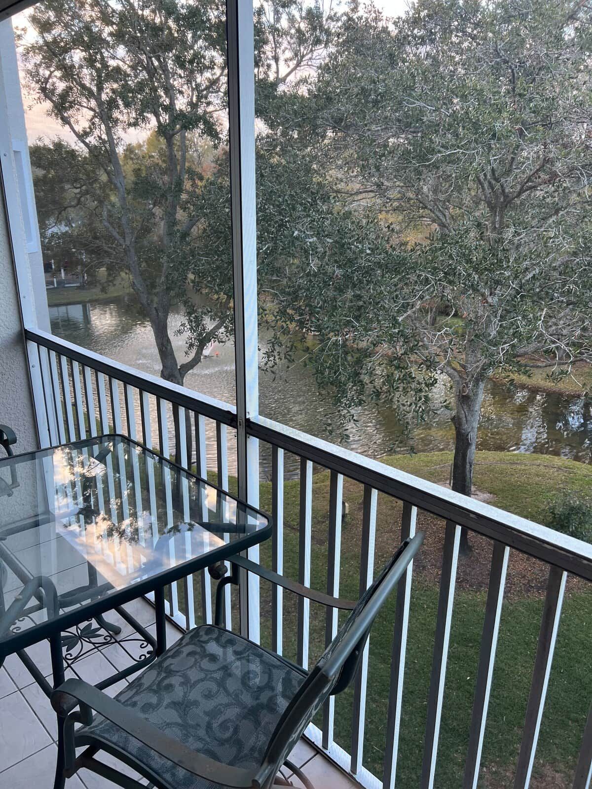 Un balcón con una mesa y sillas de vidrio, con vistas a un cuerpo de agua y árboles.