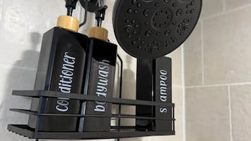 A black showerhead mounted on a wall with a black metal shelf holding two bottles labeled 'Colditor' and 'Balm'.