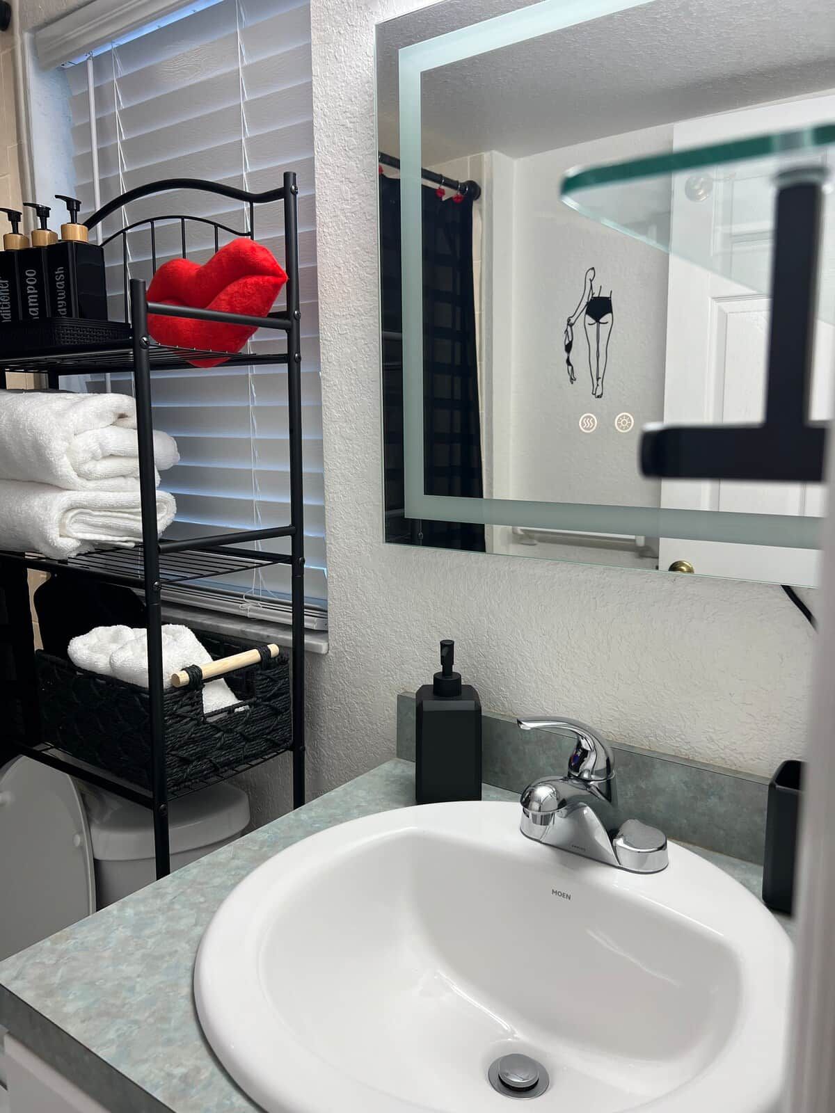 Een badkamer met een witte wasbak, een zwarte handdoekhouder met handdoeken, een spiegel en een zeepdispenser aan de muur.