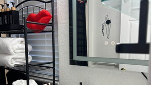 Une salle de bain avec un lavabo blanc, un porte-serviettes noir avec des serviettes, un miroir et un distributeur de savon fixé au mur.