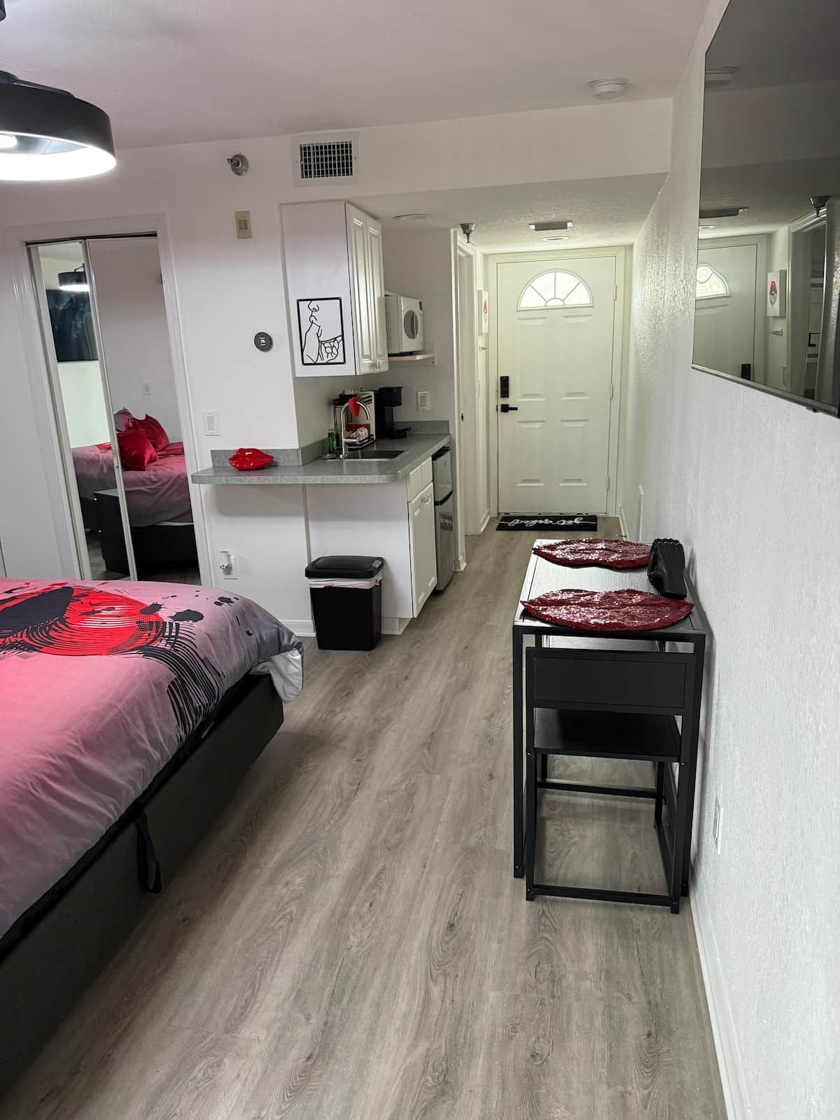 Ein kleines Hotelzimmer mit Bett, einer kleinen Küchenzeile, einem Esstisch und einem Spiegel.
