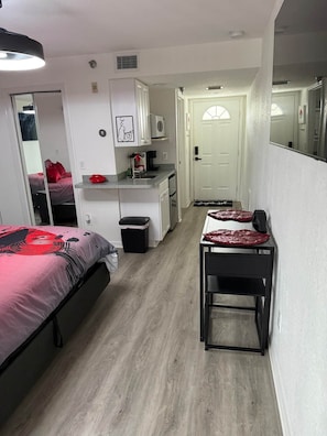 Una habitación de hotel compacta con cama, una kitchenette pequeña, una mesa de comedor y un espejo.