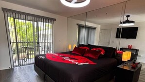 Une chambre moderne avec un grand lit, un ventilateur de plafond, une télévision et une fenêtre avec des stores.
