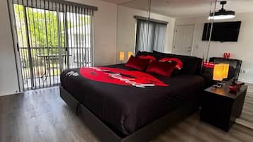Un dormitorio moderno con una cama grande, un ventilador de techo, un televisor y una ventana con persianas.