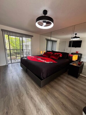 Une chambre moderne avec un grand lit, un ventilateur de plafond, une télévision et une fenêtre avec des stores.