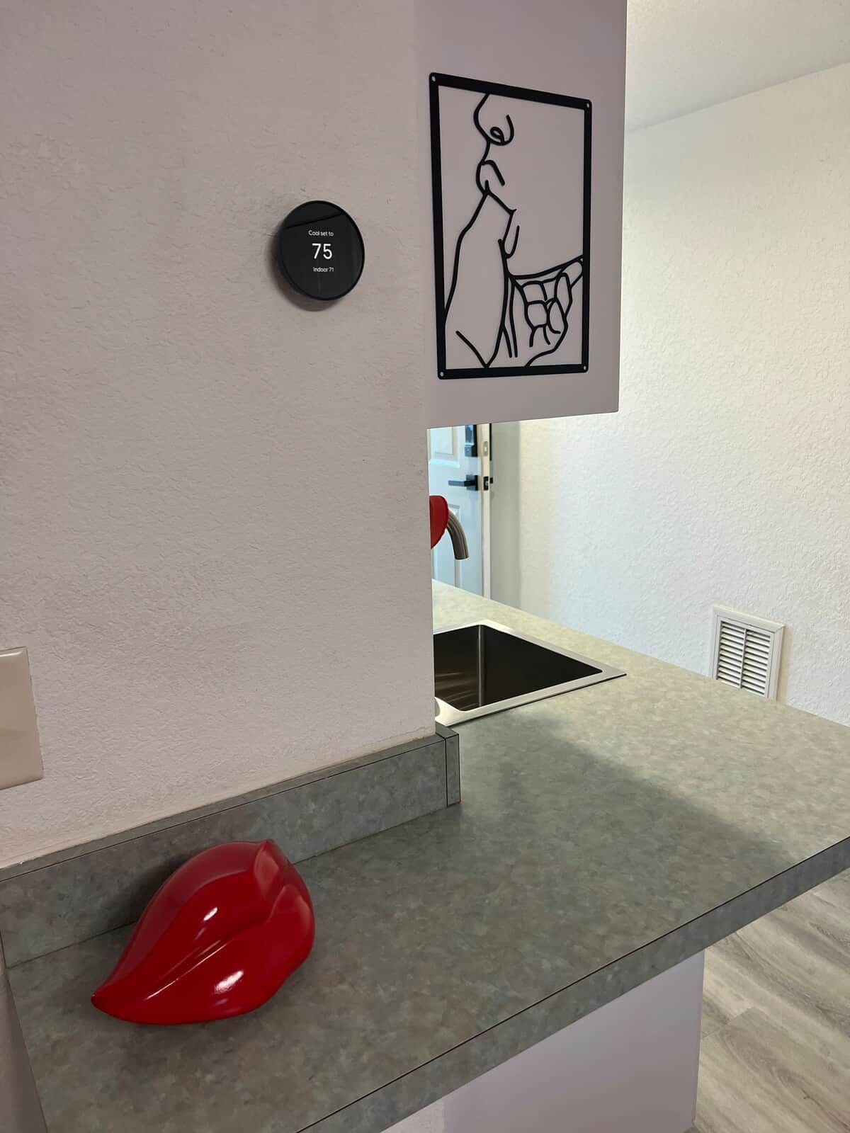 Una cuina moderna amb un taulell gris, un objecte vermell a terra i un termòstat fixat a la paret.