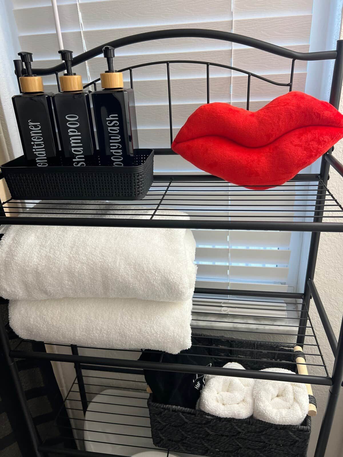 Een metalen rek met toiletartikelen, een rood kussen in de vorm van een lippenstift en opgevouwen handdoeken.