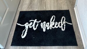 A hallway with a black doormat that reads "get naked" and a wooden floor. - Paradise Lust at Paradise Lakes Nudist resort (Lutz)