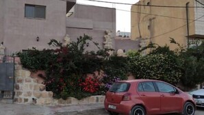 Um carro vermelho estacionado em frente a um edifício com parede de pedra e vegetação.
