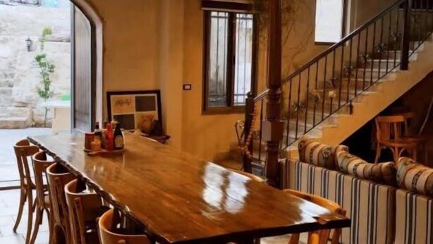 Uma ampla área de jantar com uma longa mesa de madeira e cadeiras, uma escada com corrimão e vista para o exterior.