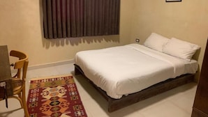 Um quarto com cama, cadeira, tapete e cortina.