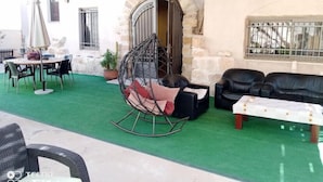 Uma área de estar ao ar livre coberta com arco de pedra, uma cadeira suspensa, uma mesa com cadeiras e um sofá.