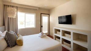 Habitación de hotel con una cama, un televisor montado en la pared y una ventana con cortinas.