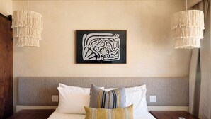 Habitación de hotel con una cama, dos mesitas de noche, una obra de arte en la pared y dos lámparas colgantes.