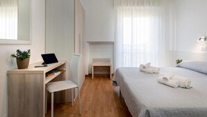 Una camera d'albergo moderna con una scrivania in legno, una sedia, un letto con asciugamani ben piegati e un piccolo tavolino.