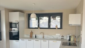 A modern kitchen with white cabinets, a black and white checkered floor, and a window with a view of trees.