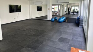 A spacious indoor area with a tiled floor, air conditioning units, exercise balls, and a visible gym area with equipment.