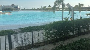 A view of a beach with clear blue water, palm trees, and a distant building.
