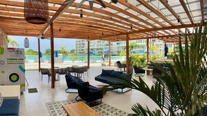 A covered outdoor seating area with wooden furniture, a pool view, and a sign advertising a purchase with confidence.