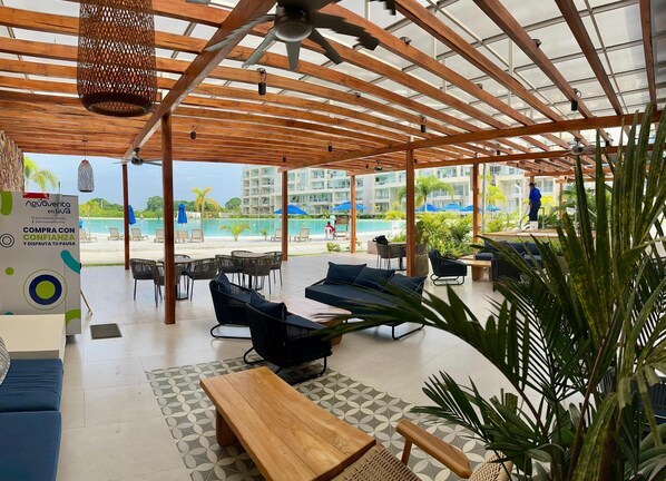 A covered outdoor seating area with wooden furniture, a pool view, and a sign advertising a purchase with confidence.