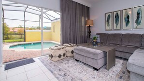 A modern living room with a grey sofa, a coffee table, and a pool view.