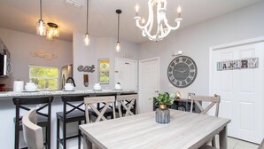 A kitchen with a wooden table, chairs, pendant lights, a chandelier, a clock, and a sign that reads "cafe".