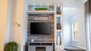 A modern living room with a fireplace, a flat-screen TV mounted above it, and a sign that reads "DisneyWorld 6 Miles."