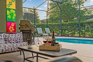 A poolside area with a sofa, a table with a tray of wine glasses and a bottle, and a bicycle. - 5BR Family Home with Private Pool Solterra Resort (Davenport)