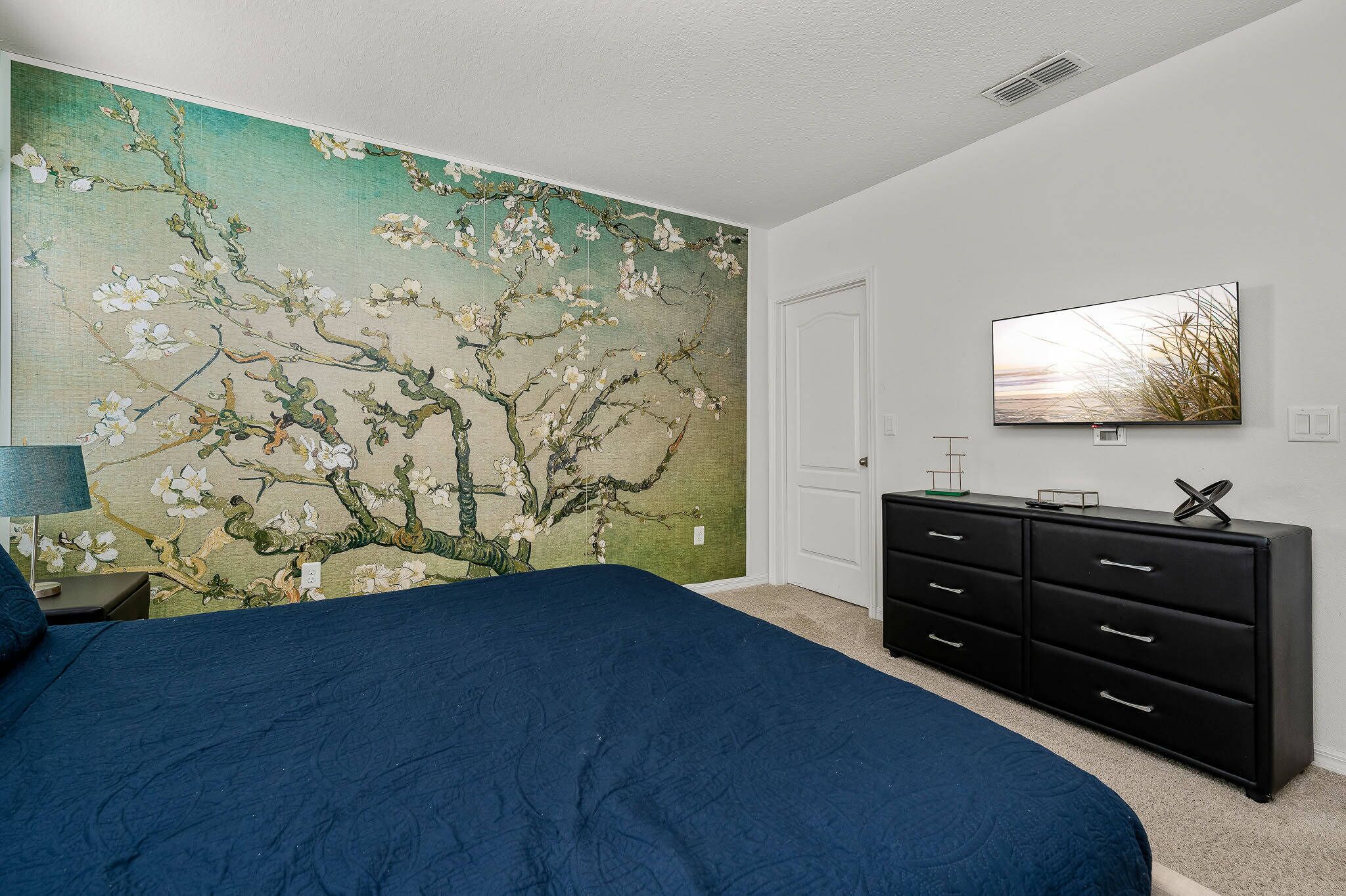 A bedroom with a large bed, a dresser, a television, and a wall mural.