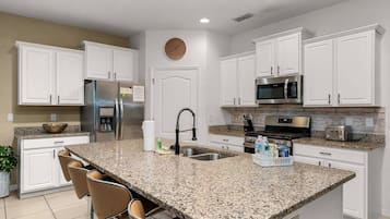 A modern kitchen with white cabinets, granite countertops, a stainless steel refrigerator, a microwave, and a sink.
