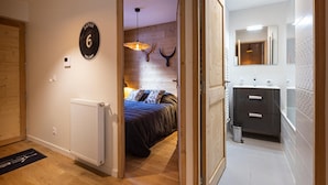 Een slaapkamer met een bed, een radiator, een houten deur en een gang naar een badkamer.