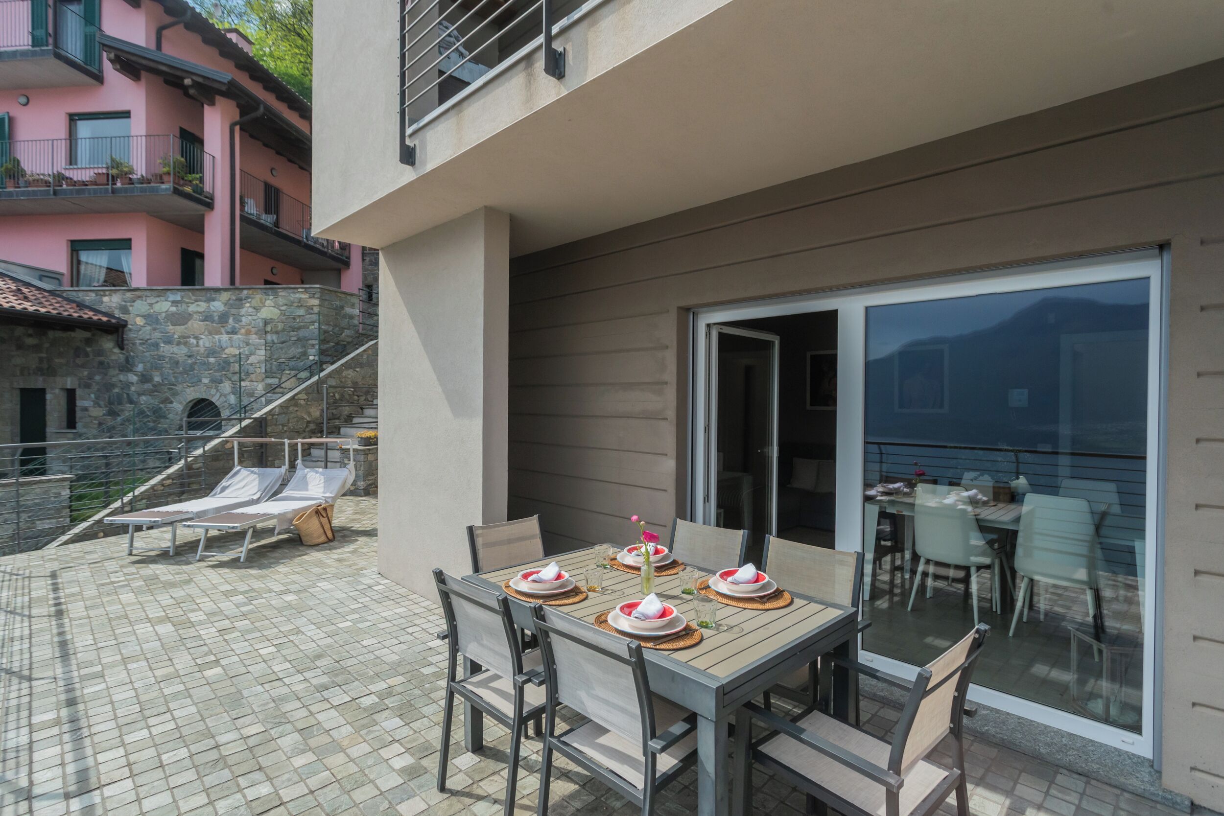 A patio with a table set for four, outdoor chairs, and a stone staircase leading to an upper level.