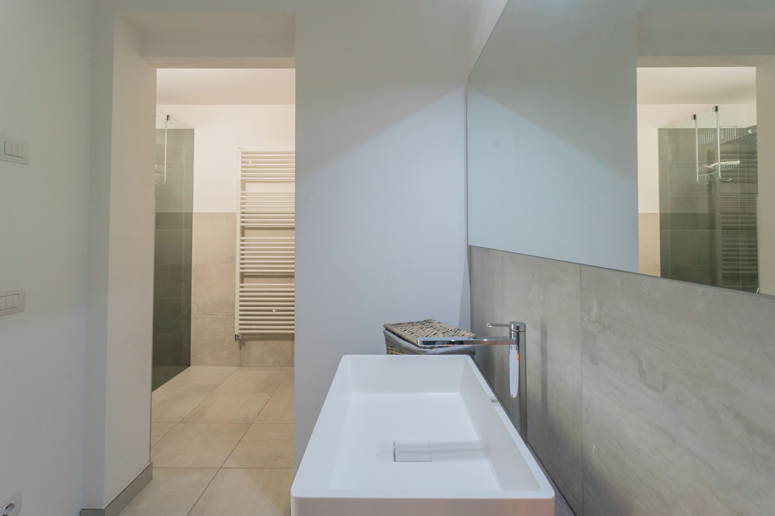 Une salle de bain moderne avec un grand miroir, un lavabo blanc et un porte-serviettes.