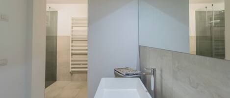 Une salle de bain moderne avec un grand miroir, un lavabo blanc et un porte-serviettes.