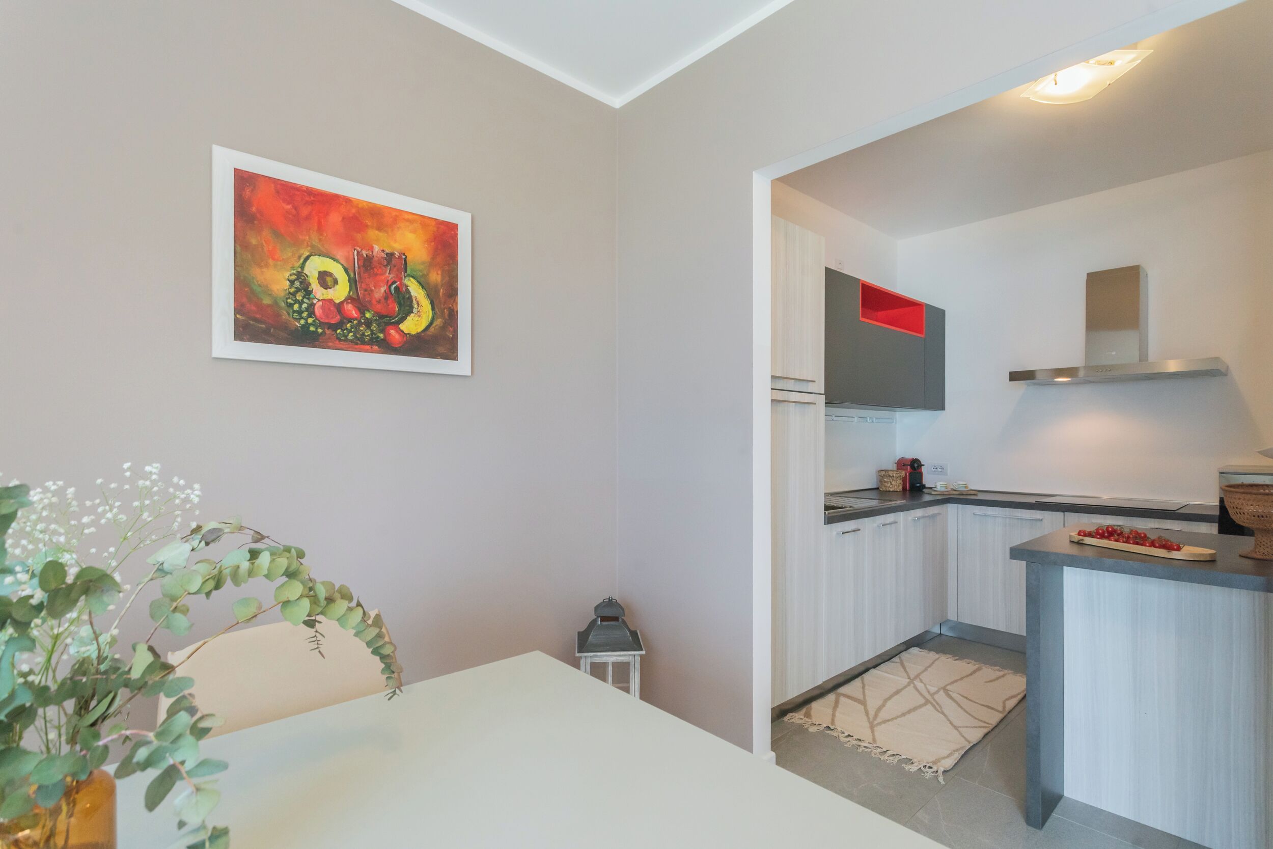 A modern kitchen with white cabinets, a grey countertop, and a red accent.
