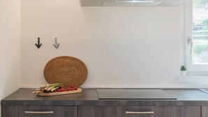 A kitchen with a modern design, featuring a stainless steel range hood, a woven basket, and a wooden cutting board with vegetables.