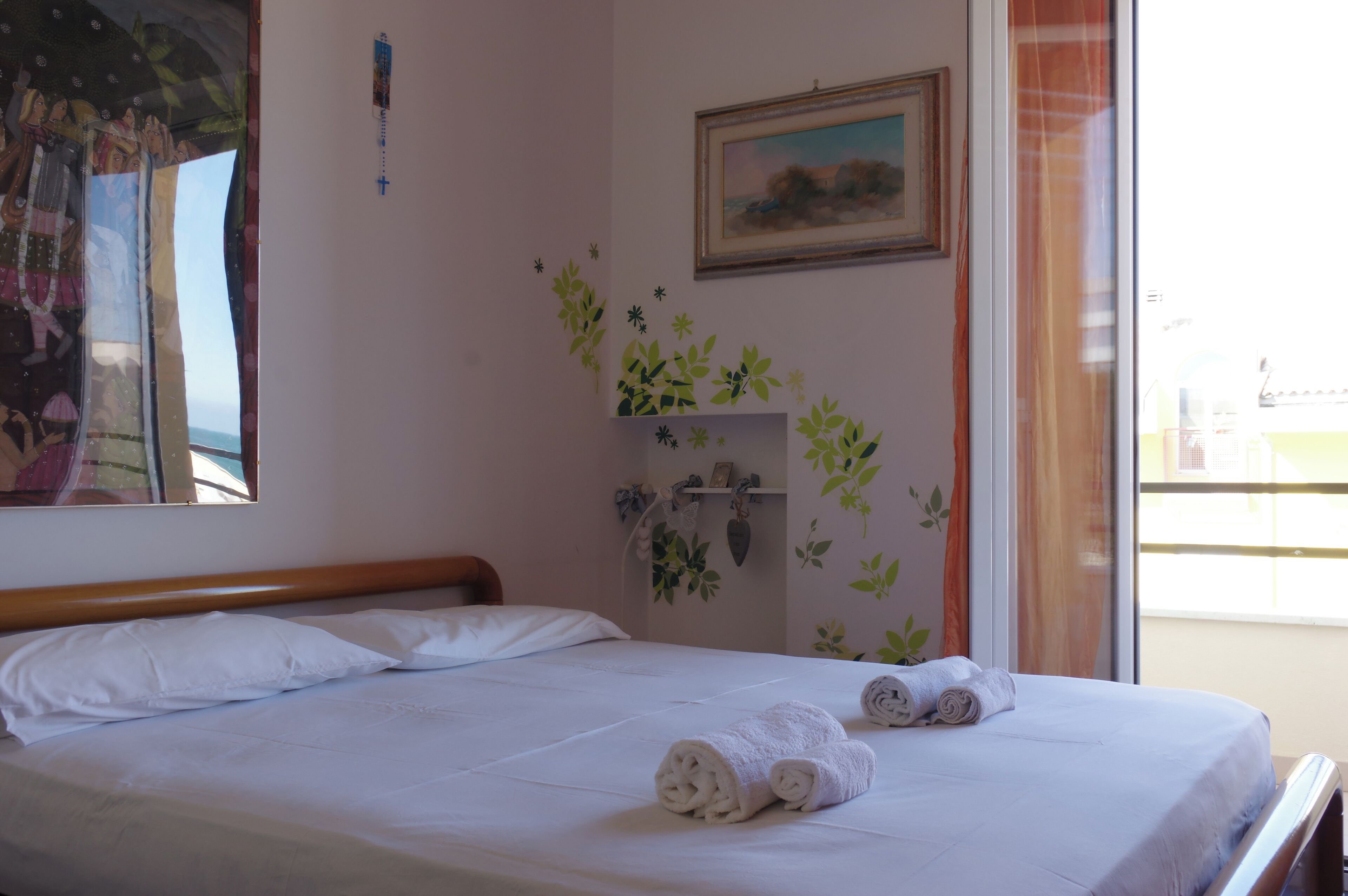 A hotel room with a bed, a small plant on a shelf, and a window with curtains.